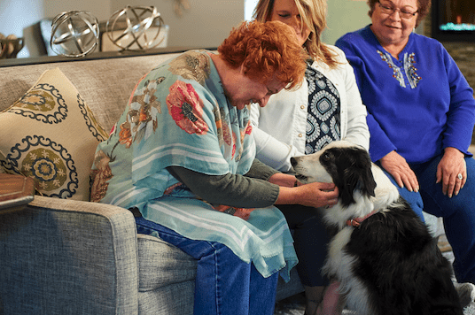 Three Senior Women sitting on a couch petting a dog in our independent living residences