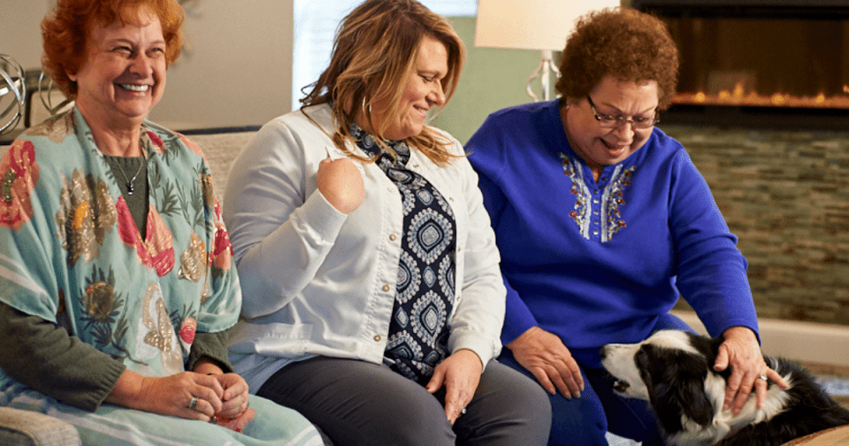 Three Senior Women sitting on a couch petting a dog