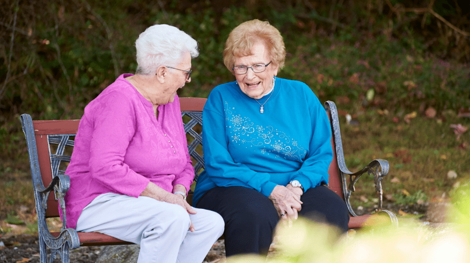 Two senior women sitting and laughing on a bench.